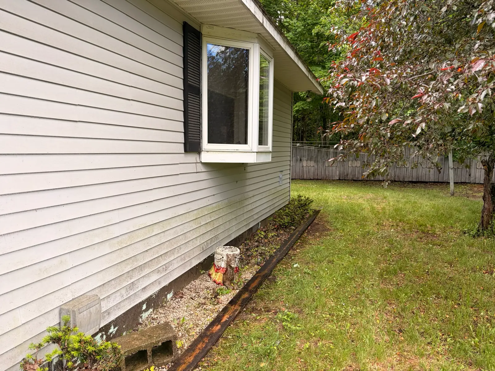 Greige vinyl siding around a bay window streaked with dirt and grime before a soft wash